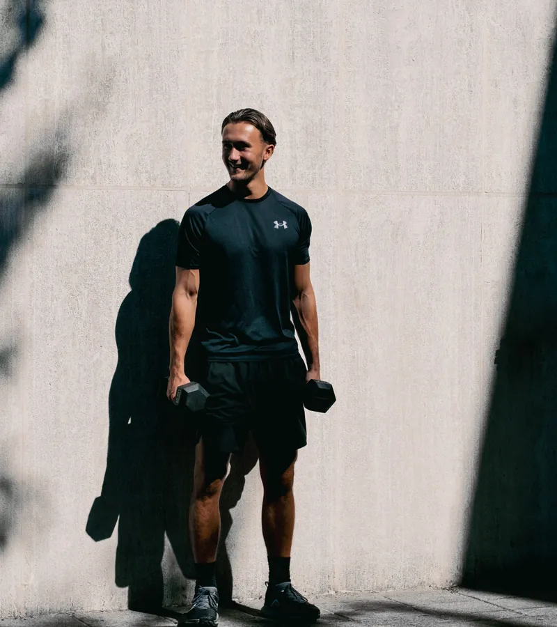 Sporter met dumbbells tegen een zonnige betonnen muur
